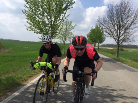 Zwei Fahrer nebeneinander auf einem Radweg zwischen Feldern, einer mit Lenkertasche