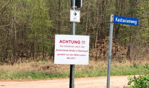 Ein Schild am Straßenrand: „Achtung!!! Sie befahren jetzt die schlechteste Straße in Oberhavel“, daneben das Schild „Kastanienweg“