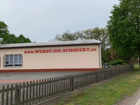 Eine Lagerhalle am Straßenrand mit der Aufschrift „www.wurst-die-schmeckt.de“