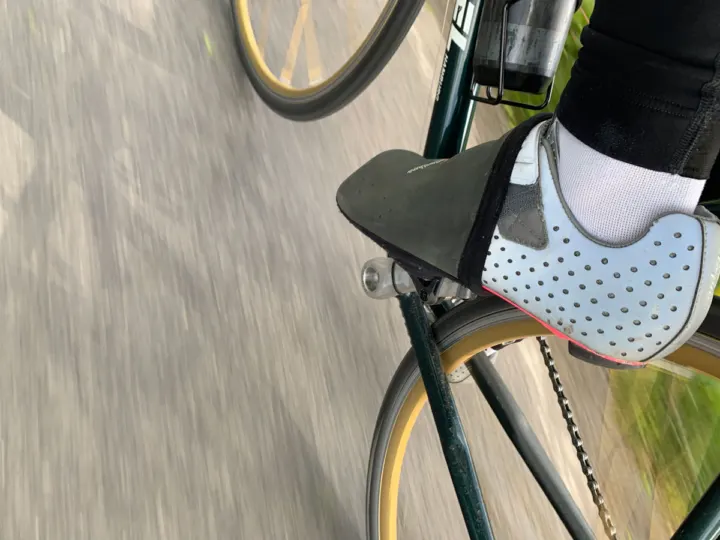 Nahaufnahme eines Fahrradschuhs mit weißem Überschuh auf dem Pedal während der Fahrt
