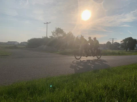 Fahrer auf einer Landstraße im Gegenlicht der tief stehenden Sonne, lange Schatten auf dem Asphalt
