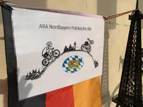 Ein Banner „ARA Nordbayern Fränkische Alb“ mit gezeichneten Radfahrern über einem Berg