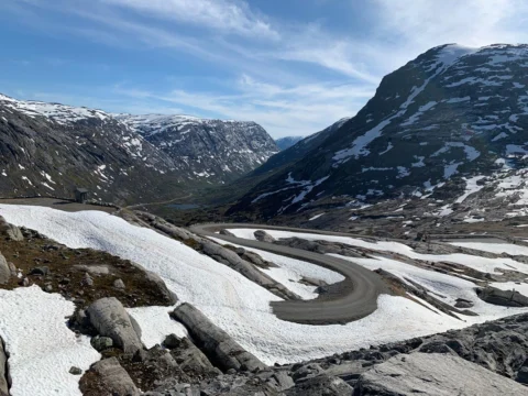 Serpentinen einer Passstraße durch ein weites Schneefeld, dahinter kahle Berge