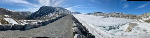 Die Straße führt zwischen Schneewänden hindurch, dahinter ein zugefrorener See