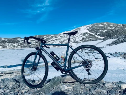 Ein Gravelbike auf Geröll am Ufer des gefrorenen Sees unter tiefblauem Himmel