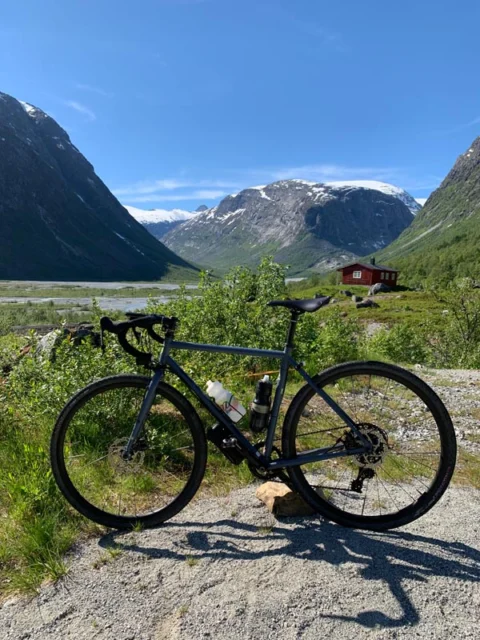 Ein Gravelbike am Schotterrand, dahinter ein weites Gletschertal mit Schneefeldern