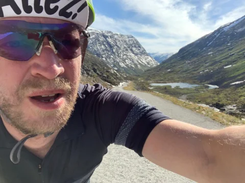 Ein Radfahrer macht ein Selfie, hinter ihm ein Tal mit steilen Felswänden und Wasserfällen