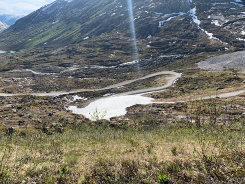 Eine schmale Straße windet sich durch karge Hochebene mit Schneeresten und Schmelzbächen