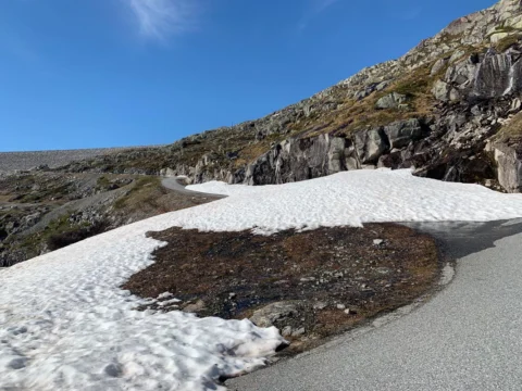 Die Straße führt an einer Schneewechte vorbei über kahlen Fels unter tiefblauem Himmel