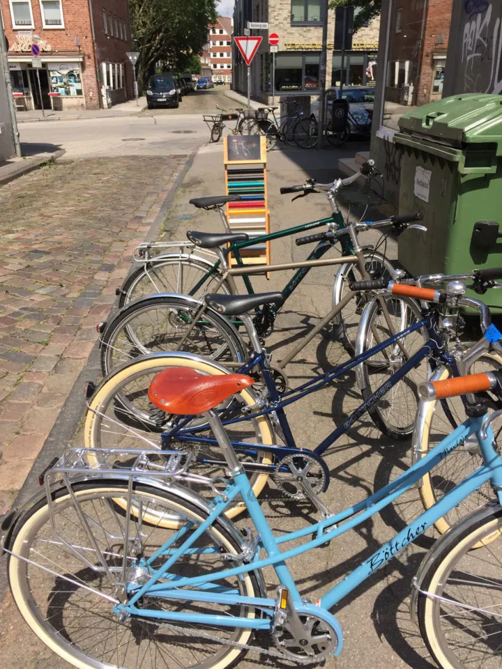 Eine Reihe bunter Böttcher-Räder am Straßenrand, vorn ein hellblaues mit orangem Sattel
