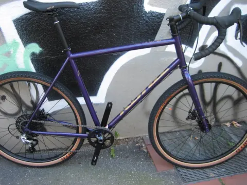Das Kona Rove ST in Violett von der linken Seite an einer Graffitiwand