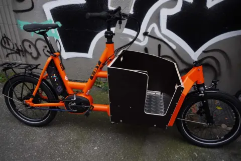 Das i:SY Cargo N3.8 ZR in Orange von der linken Seite, mit Transportbox über dem Vorderrad