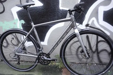 Das Scott Metrix 30 EQ in Grau von der linken Seite an einer Graffitiwand
