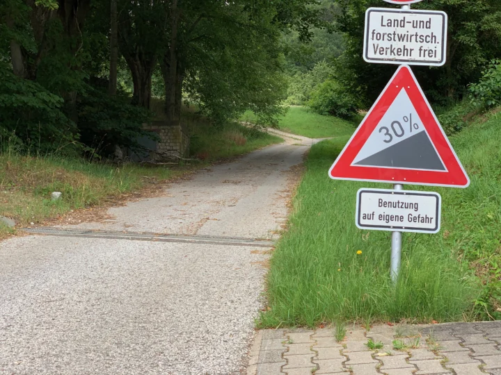 Ein Waldweg mit Warnschild „30 % Gefälle“ und dem Zusatz „Benutzung auf eigene Gefahr“