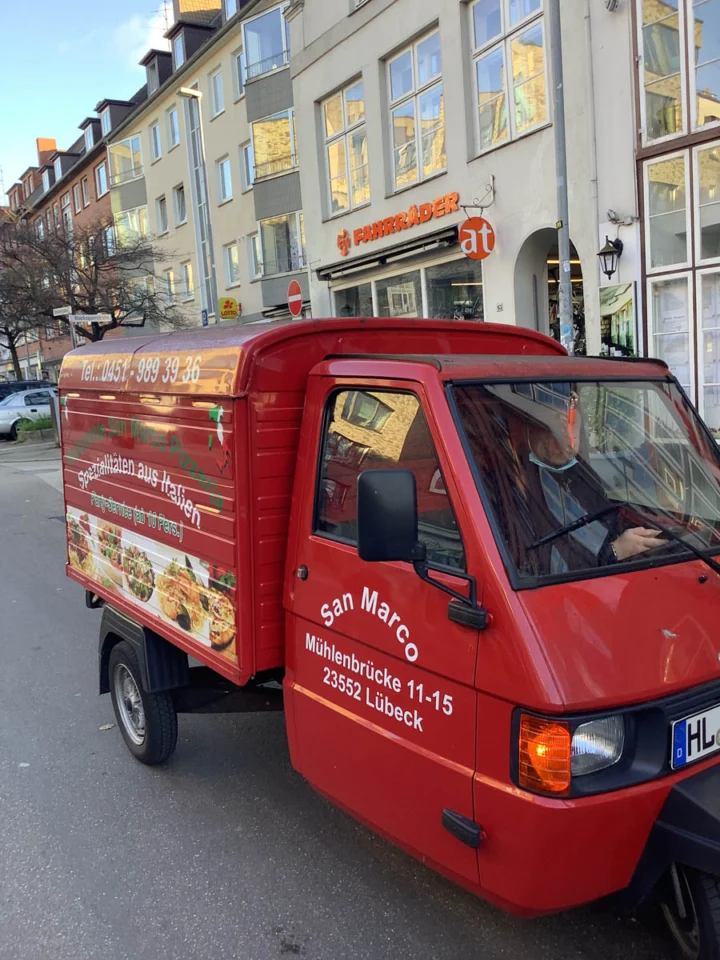 Eine rote Ape mit Pizzawerbung parkt an einer Lübecker Straße