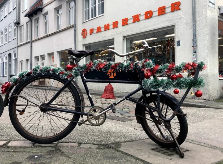 Ein altes Lastenrad vor dem Laden, über der Ladefläche Tannengirlanden mit roten Kugeln und einer Glocke