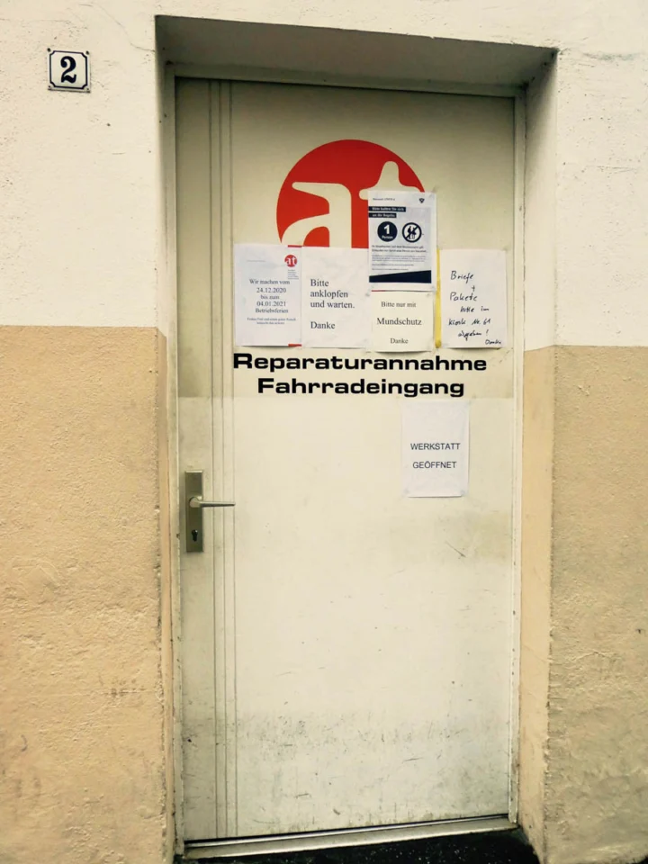 Die Tür der Reparaturannahme mit dem at-Logo und mehreren angehefteten Hinweiszetteln
