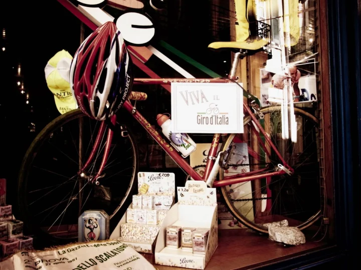 Ein Schaufenster mit rotem Rennrad, Helm und Panettone-Schachteln, dazwischen ein Schild „Viva il Giro d'Italia“