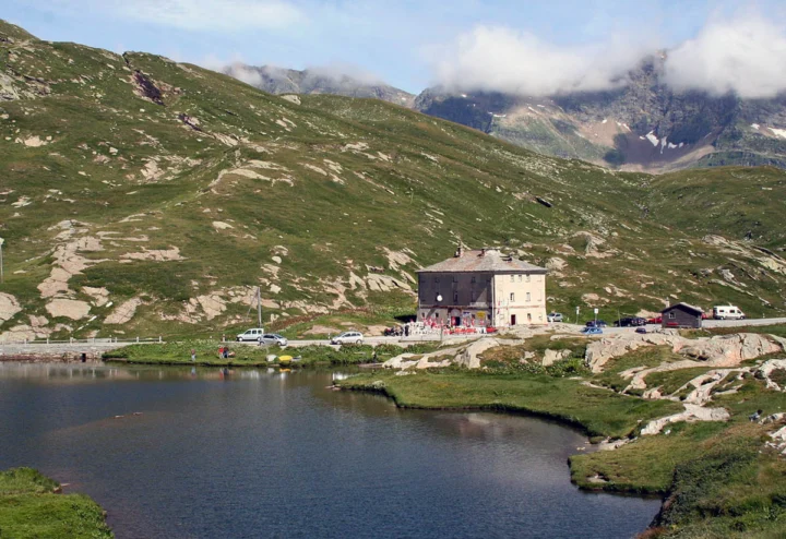 Ein Bergsee unter Wolken, am Ufer ein steinernes Haus, ringsum karge Almhänge