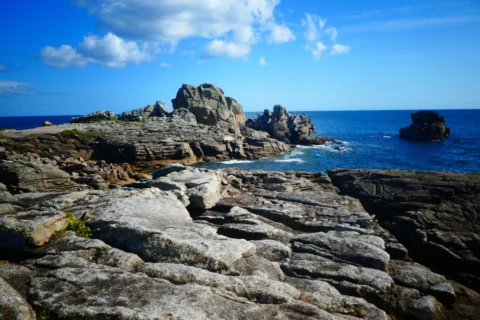 Abgeschliffene Granitplatten an der Küste, dahinter Felsklippen und das offene Meer unter Schäfchenwolken