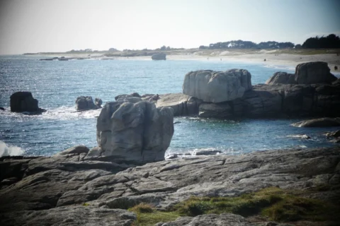 Granitblöcke an der bretonischen Küste, dahinter eine Bucht und ein heller Sandstrand