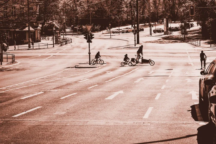 Eine weite Straßenkreuzung in Sepia, darauf einzelne Radfahrende und Fußgänger