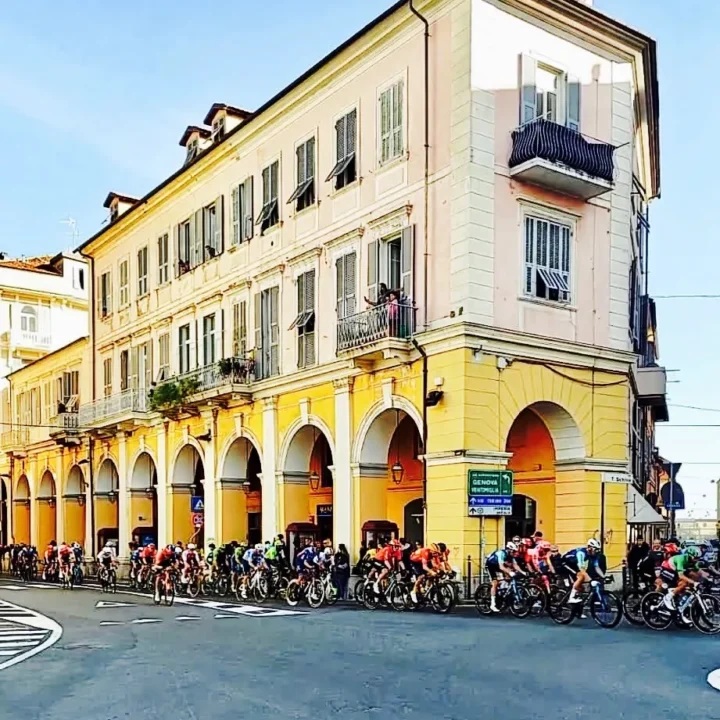 Das Feld fährt an einem gelben Arkadenhaus vorbei durch eine italienische Kleinstadt