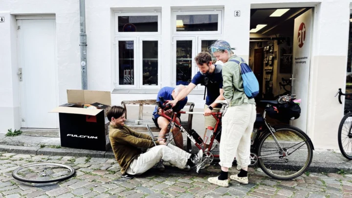 Vor dem Laden richtet jemand die Gabel eines Tandems, zwei weitere schauen zu
