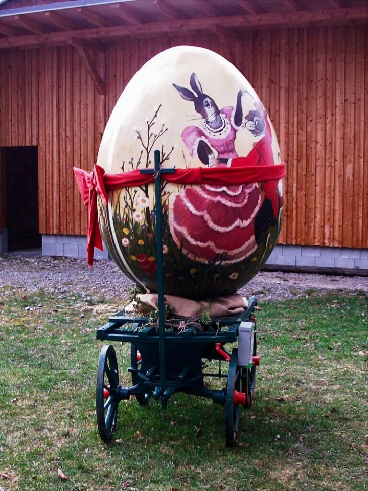 Ein übergroßes bemaltes Osterei mit Hasenmotiv auf einem alten Handwagen