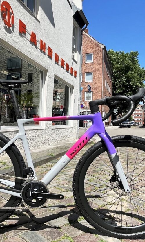 Das 2025er Scott Addict Gravel 20 in M und der bunten Lackierung narwal grey/fade purple - ein farbenfrohes Gravel Bike jetzt bei at Fahrräder, deinem Fahrradladen in Lübeck, mit Fahrradwerkstatt und Liebe zum Fahrrad, zum Radsport und zum Rennrad