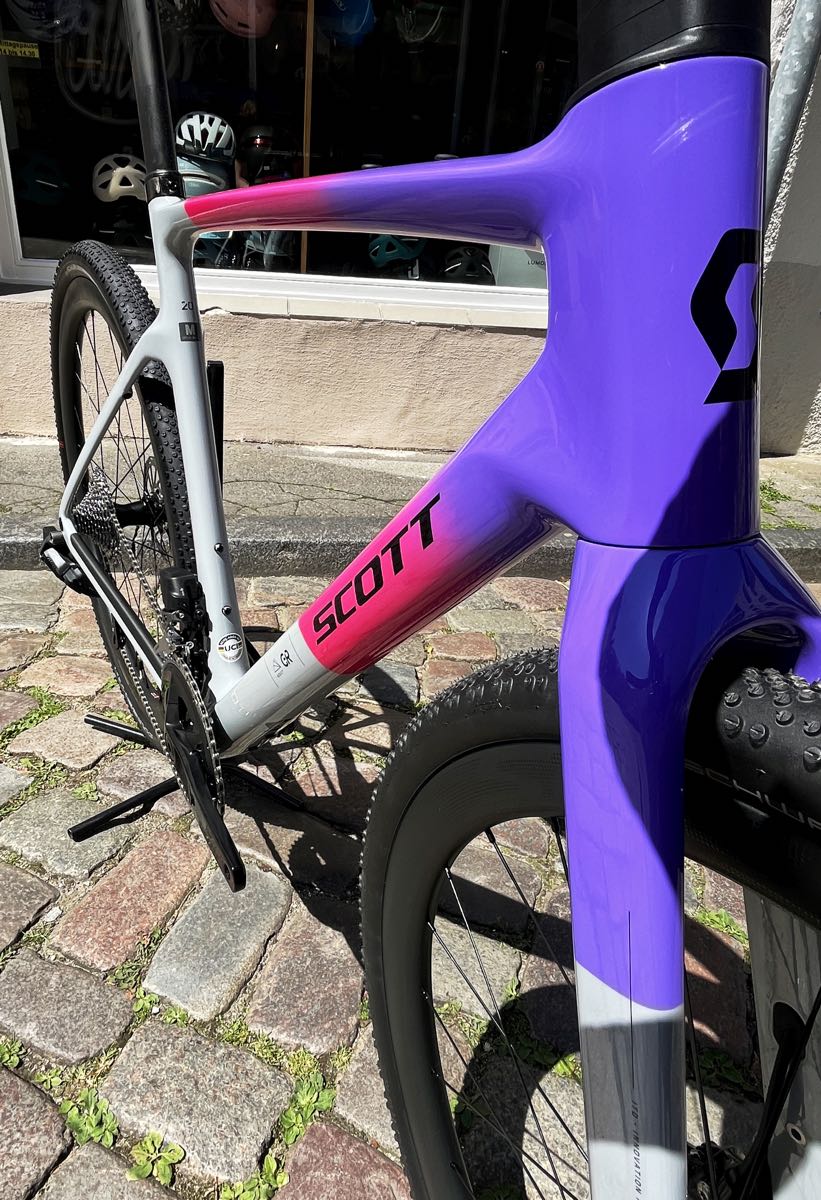 Das 2025er Scott Addict Gravel 20 in M und der bunten Lackierung narwal grey/fade purple - ein farbenfrohes Gravel Bike jetzt bei at Fahrräder, deinem Fahrradladen in Lübeck, mit Fahrradwerkstatt und Liebe zum Fahrrad, zum Radsport und zum Rennrad