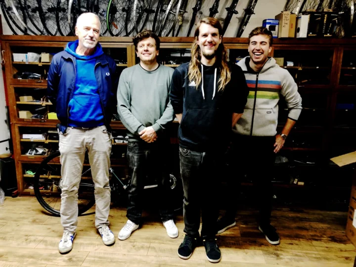 Dieselben vier Mitarbeiter, diesmal vor der Regalwand der Werkstatt
