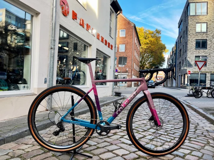 Das Colnago G3-X „Purple Rain“ mit violett-blauem Verlauf steht vor dem Schaufenster des Ladens