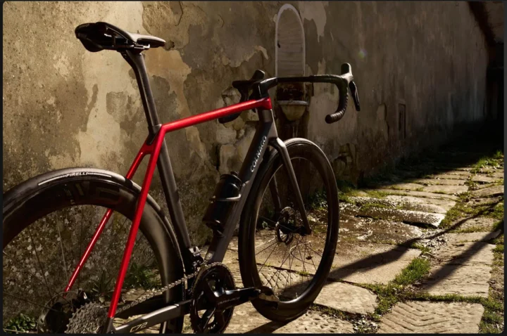 Ein schwarz-rotes Colnago C72 lehnt an einer alten Mauer im Streiflicht