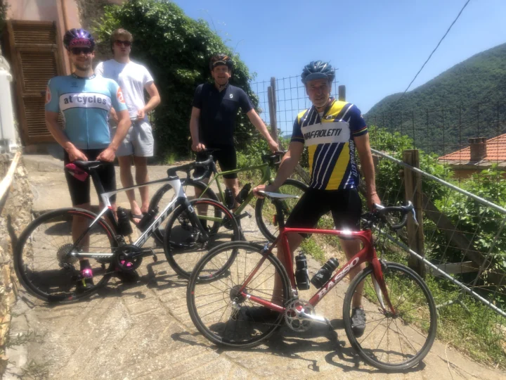 Jonathan im at-cycles-Trikot, Daniel, Fabian und Jens mit ihren Rennrädern auf einem Dorfweg