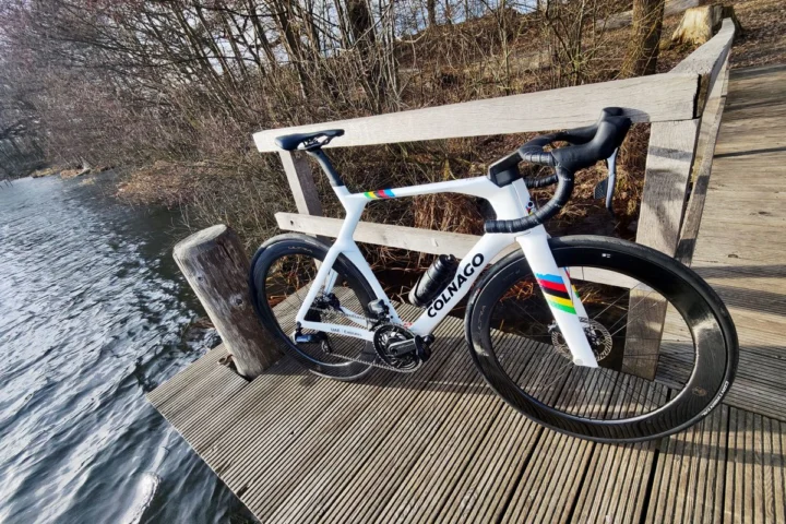 Ein weißes Colnago Y1 RS mit Regenbogenstreifen lehnt an einer Bank am Wasser