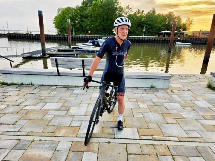 Ein Radfahrer steht mit seinem Rennrad an einer Hafenpromenade im Abendlicht
