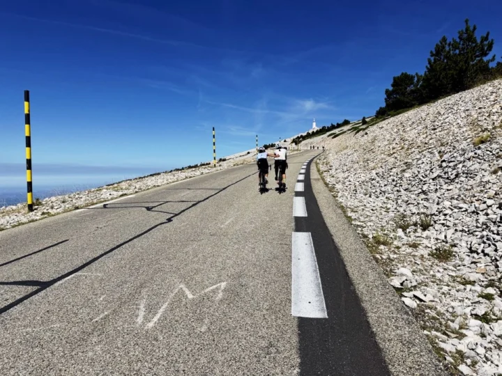 Zwei Radfahrende dicht nebeneinander auf der letzten Rampe zum Gipfel, links die schwarz-gelben Schneestangen